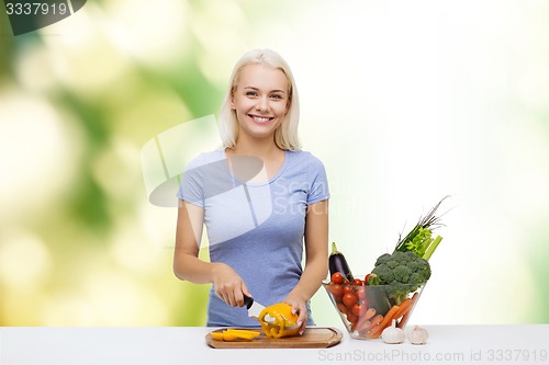 Image of smiling young woman chopping vegetables at home