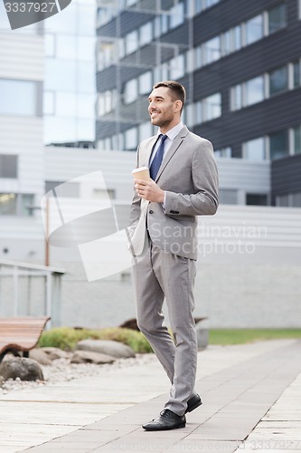 Image of young serious businessman with paper cup outdoors