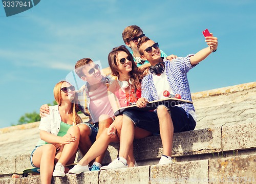 Image of group of smiling friends with smartphone outdoors