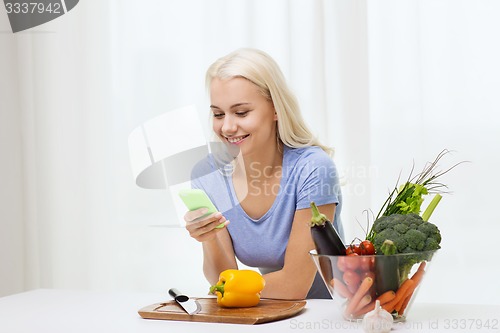 Image of smiling woman with smartphone cooking vegetables