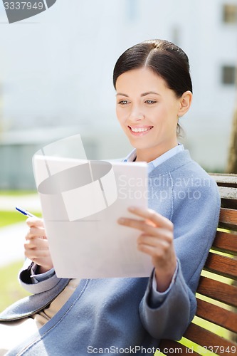 Image of smiling businesswoman reading papers outdoors