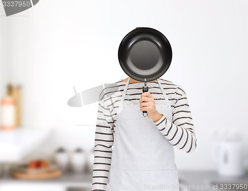 Image of man or cook in apron hiding face behind frying pan