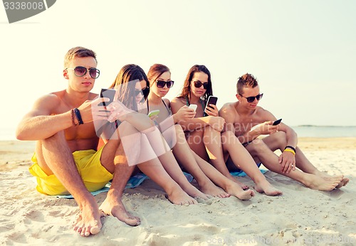 Image of group of friends with smartphones on beach