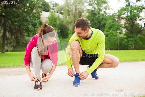 Image of smiling couple tying shoelaces outdoors