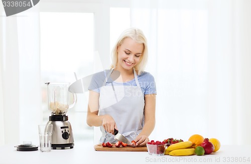 Image of smiling woman with blender preparing shake at home