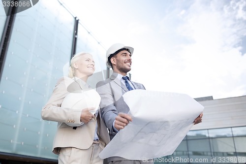 Image of smiling businessmen with blueprint and helmets