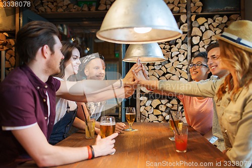 Image of happy friends with drinks making high five at bar