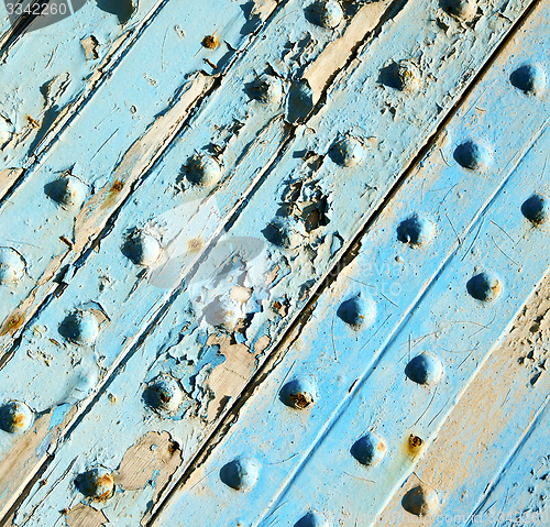 Image of dirty stripped paint in the blue wood door and rusty nail