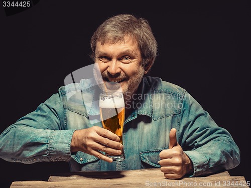 Image of The smiling man in denim shirt with glass of beer