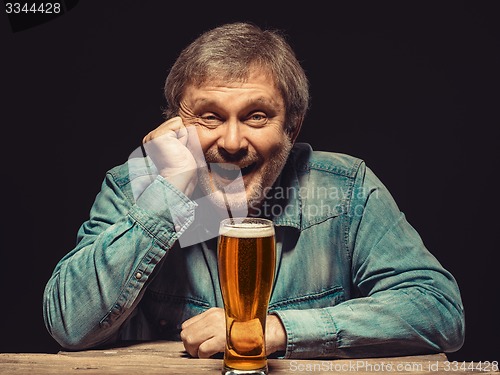 Image of The smiling man in denim shirt with glass of beer