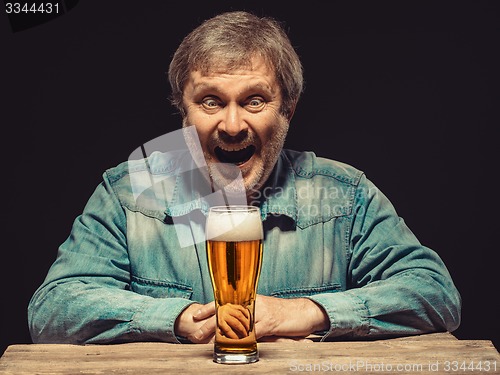 Image of The smiling man in denim shirt with glass of beer