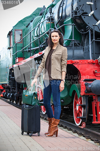 Image of adult woman traveler with a suitcase near the vintage steam loco