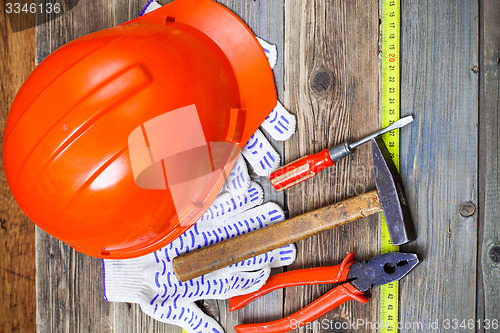 Image of aged hammer, pliers, screwdriver, tape measure, a bright helmet 