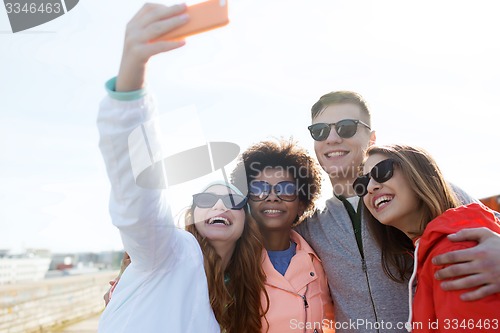 Image of smiling friends taking selfie with smartphone