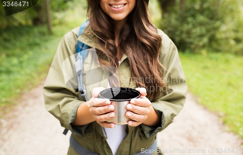 Image of smiling young woman with cup and backpack hiking