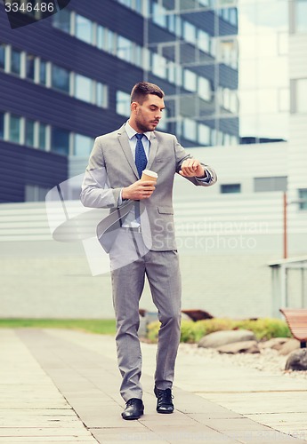 Image of young serious businessman with paper cup outdoors