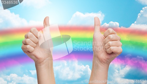 Image of hands showing thumbs up over rainbow in blue sky