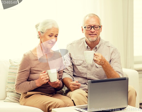 Image of happy senior couple with laptop and cups at home