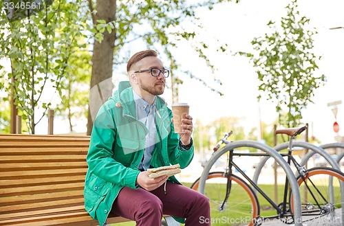 Image of happy young hipster man with coffee and sandwich