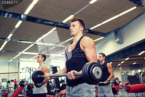 Image of group of men flexing muscles with barbell in gym