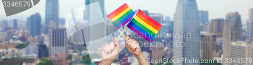 Image of hands holding rainbow flags over city background