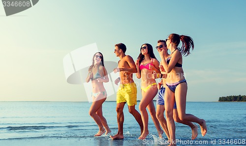 Image of smiling friends in sunglasses running on beach