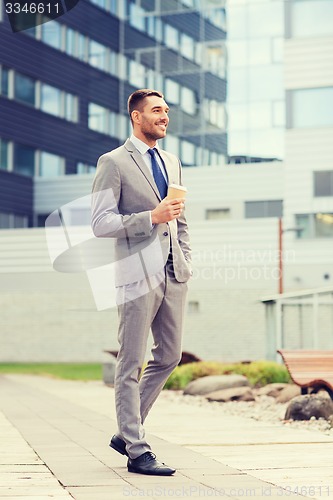 Image of young serious businessman with paper cup outdoors