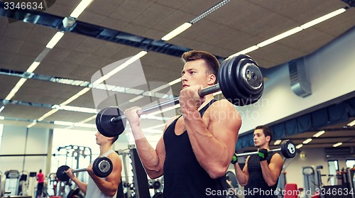 Image of group of men flexing muscles with barbell in gym