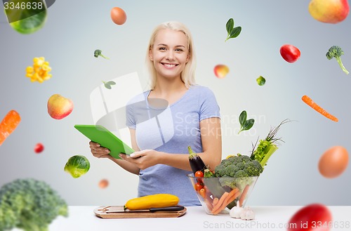 Image of smiling woman with tablet pc cooking vegetables