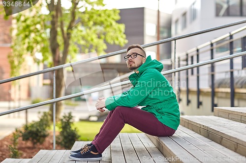 Image of happy young hipster man sitting on stairs in city