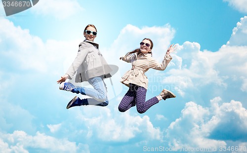 Image of happy little girls jumping high over blue sky