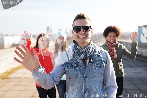 Image of happy teenage friends waving hands on city street