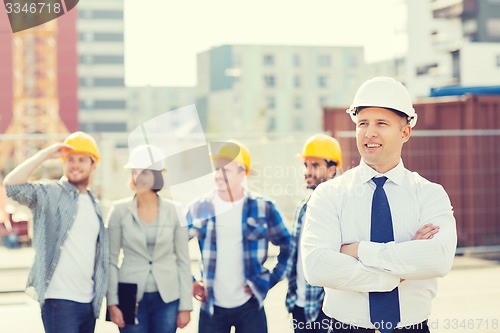 Image of group of smiling builders in hardhats outdoors