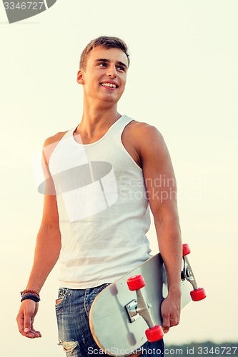 Image of smiling teenage boy with skateboard outdoors