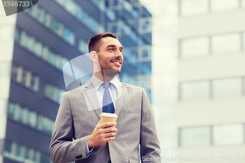 Image of young smiling businessman with paper cup outdoors