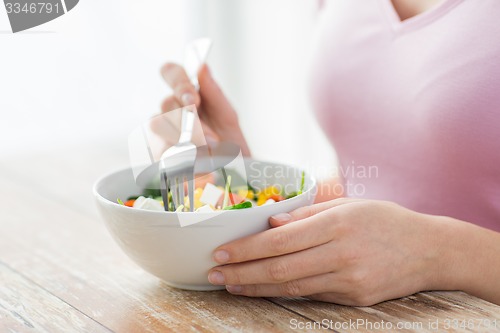 Image of close up of young woman eating salad at home