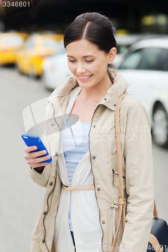 Image of smiling woman with smartphone over taxi in city