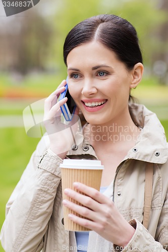 Image of smiling woman with smartphone and coffee in park