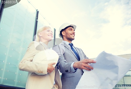 Image of smiling businessmen with blueprint and helmets