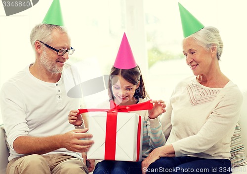 Image of smiling family in party hats with gift box at home