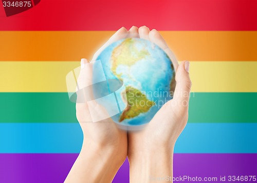 Image of close up of hands with earth globe over rainbow