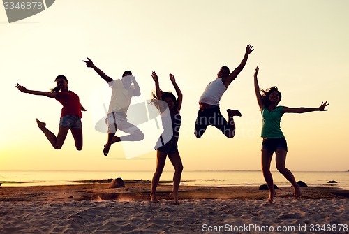 Image of smiling friends dancing and jumping on beach