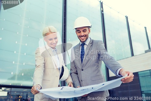 Image of smiling businessmen with blueprint and helmets