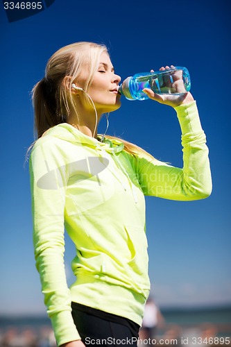 Image of woman drinking water after doing sports outdoors