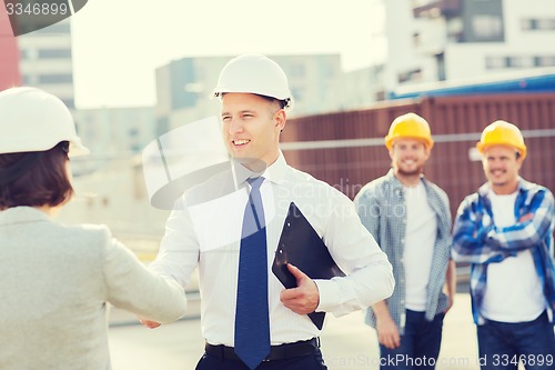 Image of group of smiling builders in hardhats outdoors