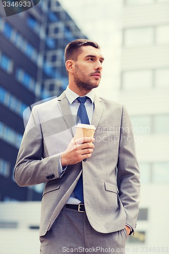 Image of young serious businessman with paper cup outdoors