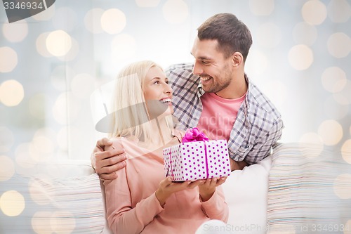 Image of happy man giving woman present over holiday lights