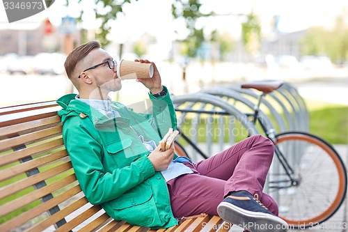 Image of happy young hipster man with coffee and sandwich