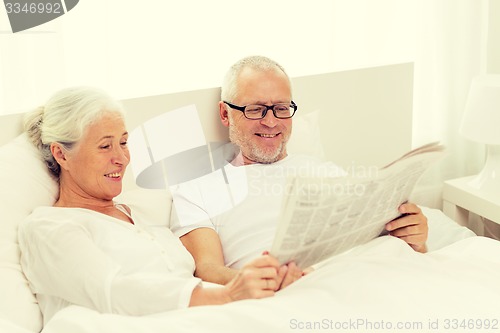 Image of happy senior couple with newspaper in bed