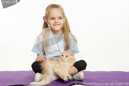 Image of Cheerful girl sitting on a rug with cat